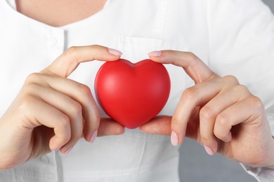 Doctor holding red heart on grey background, closeup