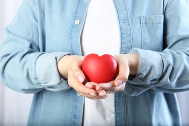 Woman holding red heart on light background, closeup