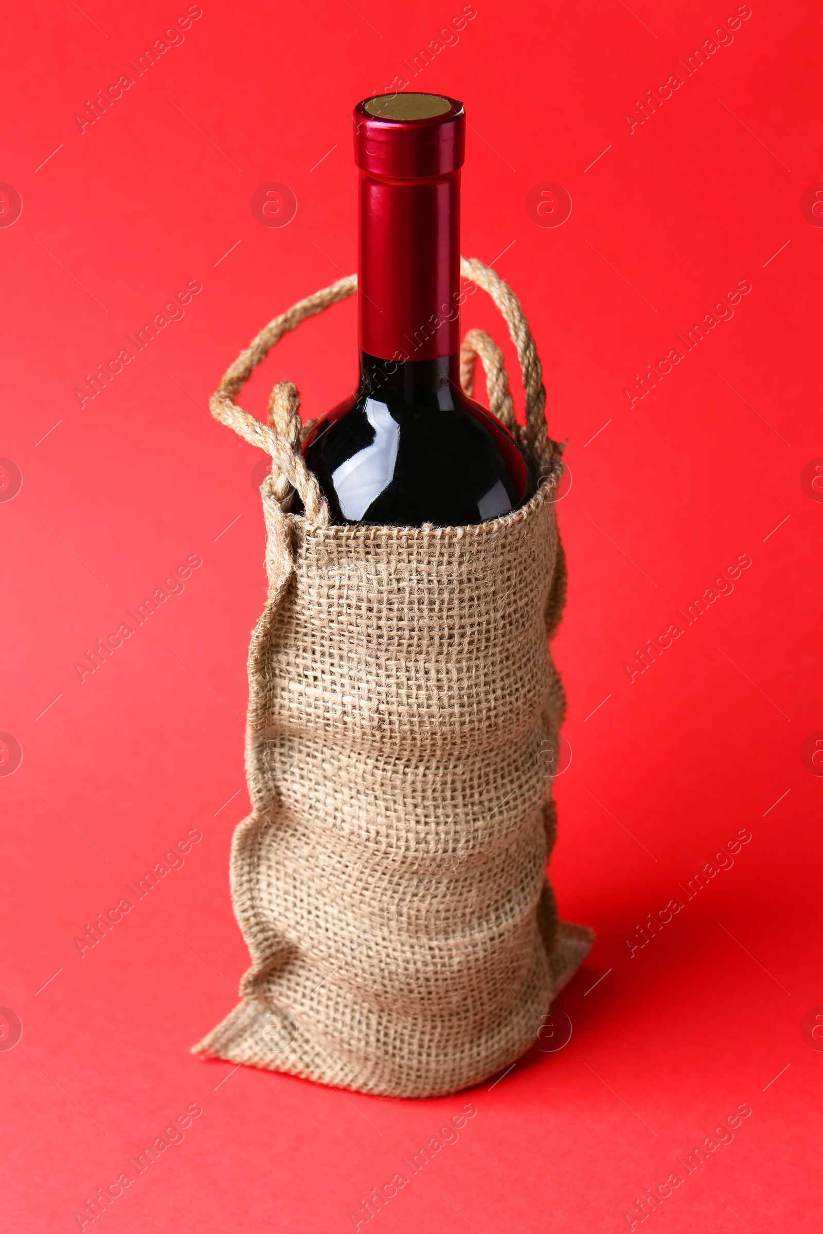 Photo of Wine bottle in burlap bag on red background