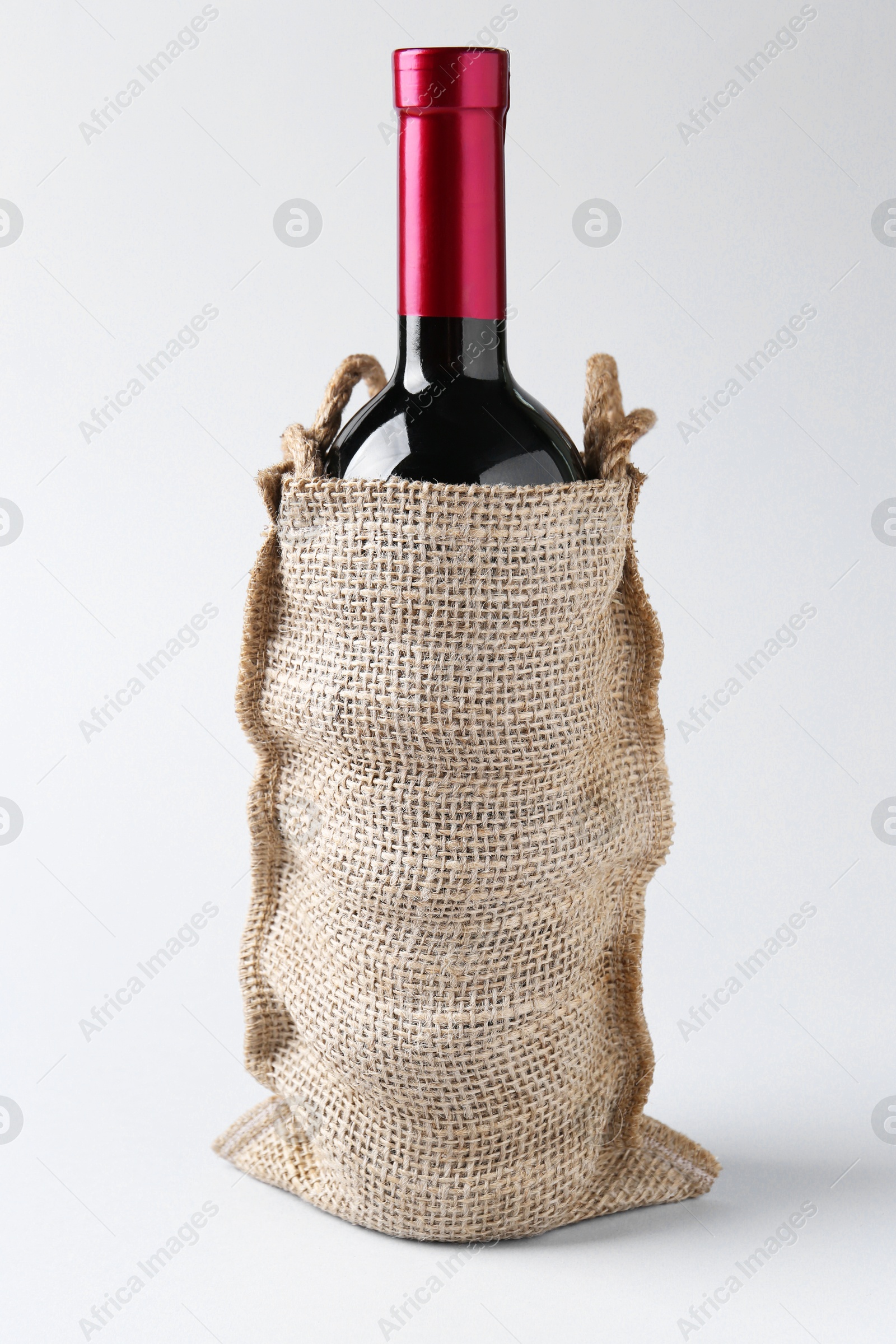 Photo of Wine bottle in burlap bag on light grey background