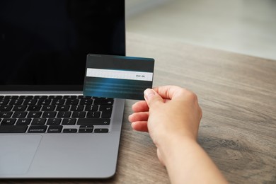 Photo of Woman with credit card using laptop at wooden table indoors, closeup