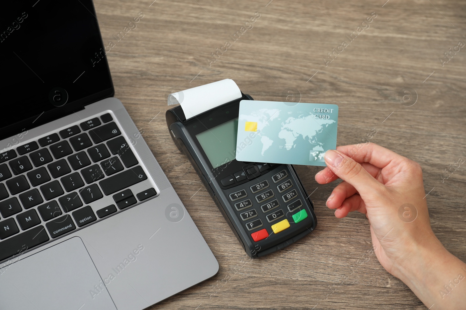 Photo of Woman with credit card using payment terminal at wooden table indoors, closeup