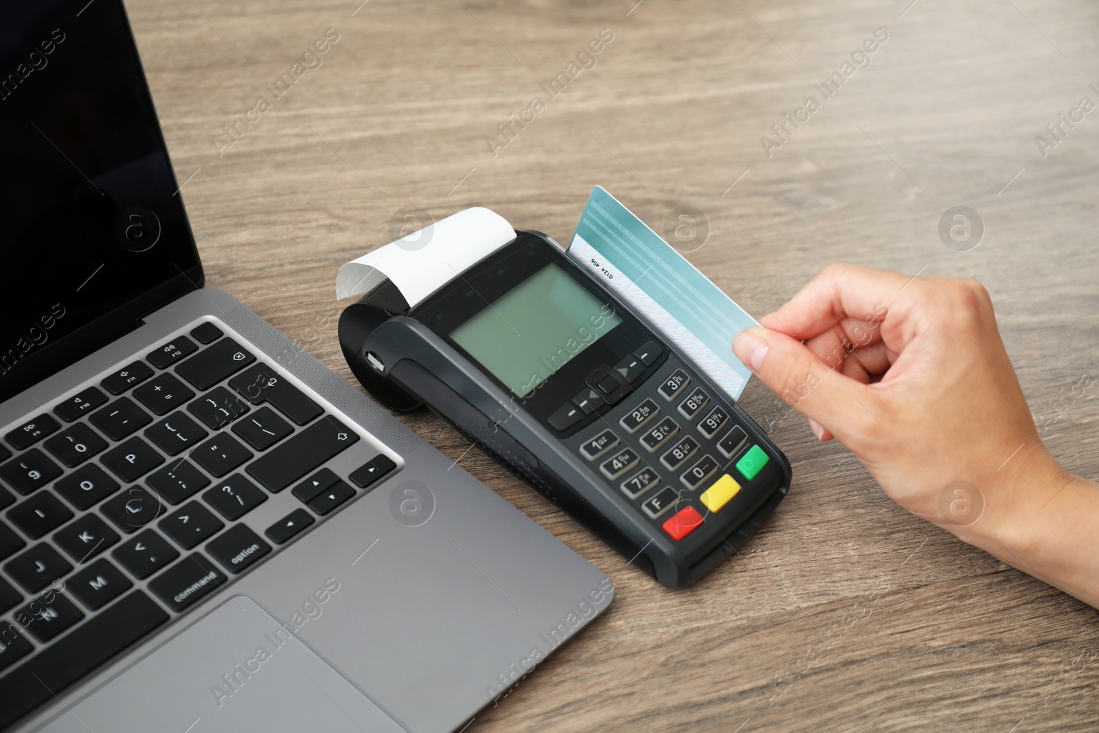 Photo of Woman with credit card using payment terminal at wooden table indoors, closeup