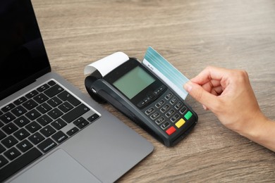 Photo of Woman with credit card using payment terminal at wooden table indoors, closeup