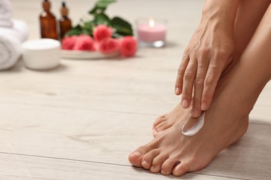 Photo of Body care. Woman applying moisturizing cream onto her feet on floor, closeup. Space for text