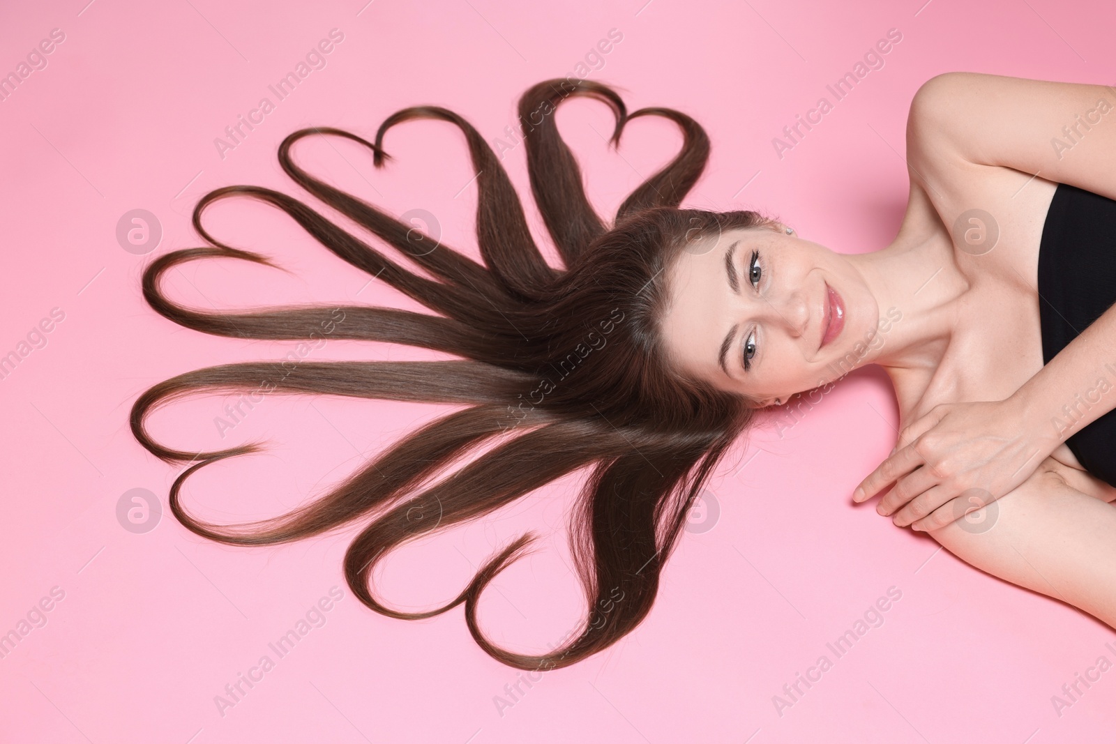 Photo of Beautiful young woman with hair in shape of hearts on pink background