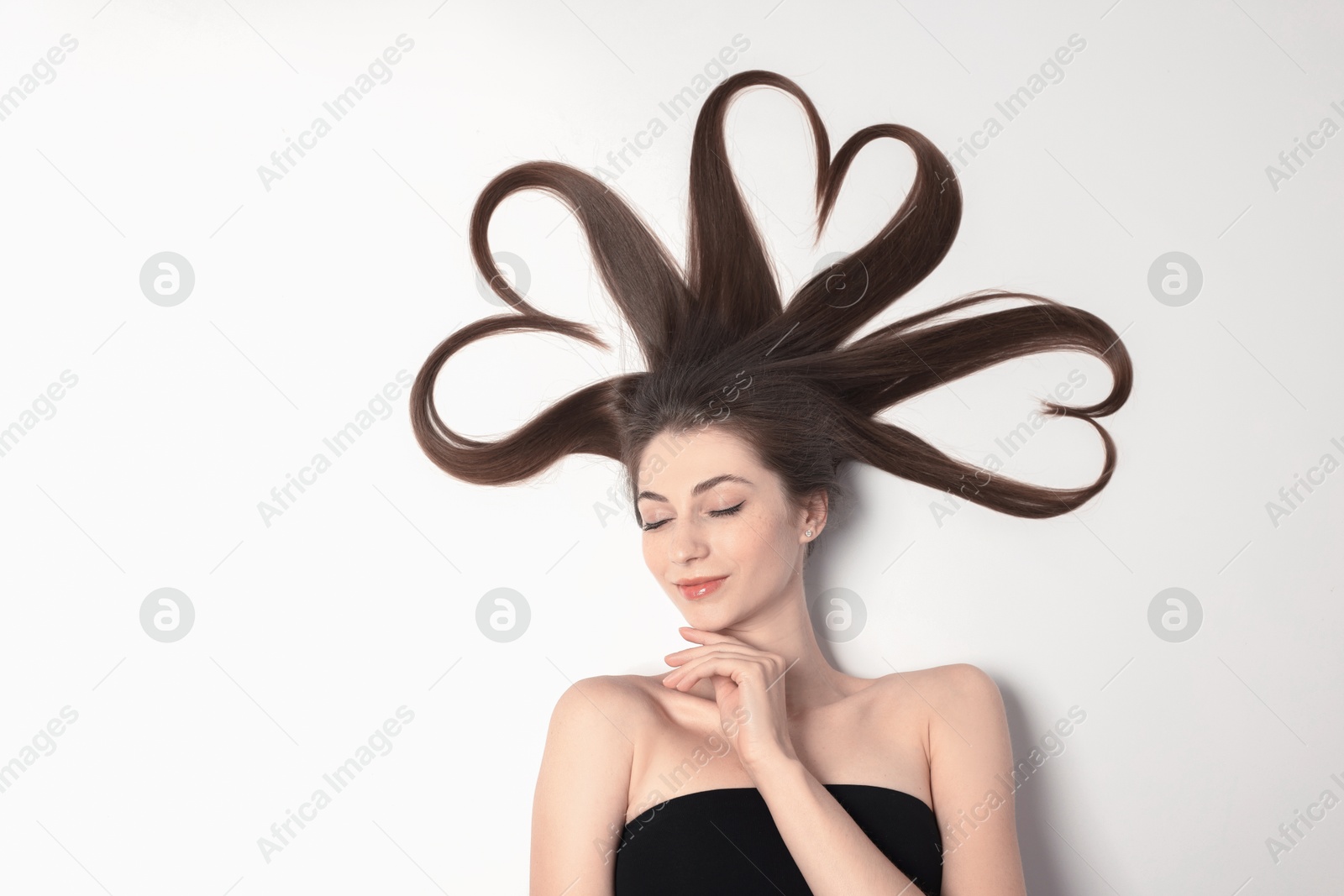 Photo of Beautiful young woman with hair in shape of hearts on white background, top view