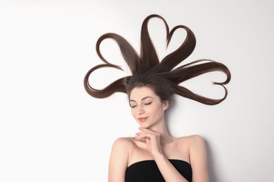 Photo of Beautiful young woman with hair in shape of hearts on white background, top view