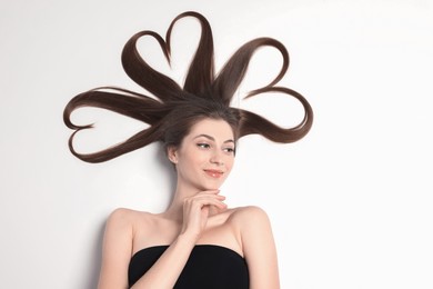 Beautiful young woman with hair in shape of hearts on white background, top view