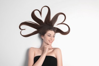 Photo of Beautiful young woman with hair in shape of hearts on white background, top view