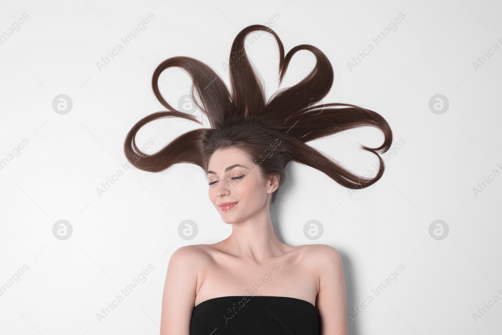 Photo of Beautiful young woman with hair in shape of hearts on white background, top view