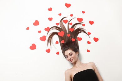 Beautiful young woman with long hair and red paper hearts on white background, top view