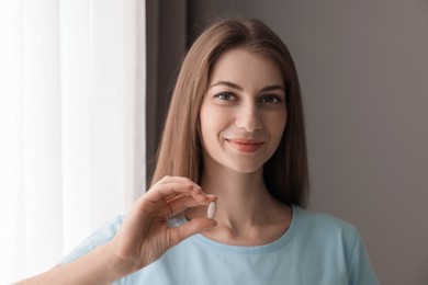 Photo of Beautiful young woman with pill at home