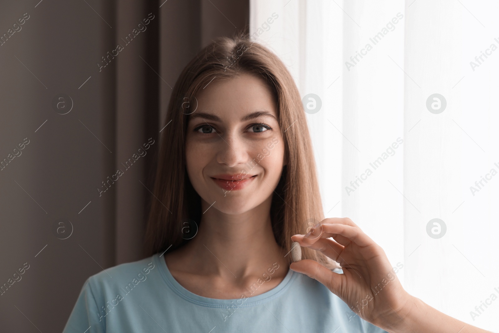 Photo of Beautiful young woman with pill at home