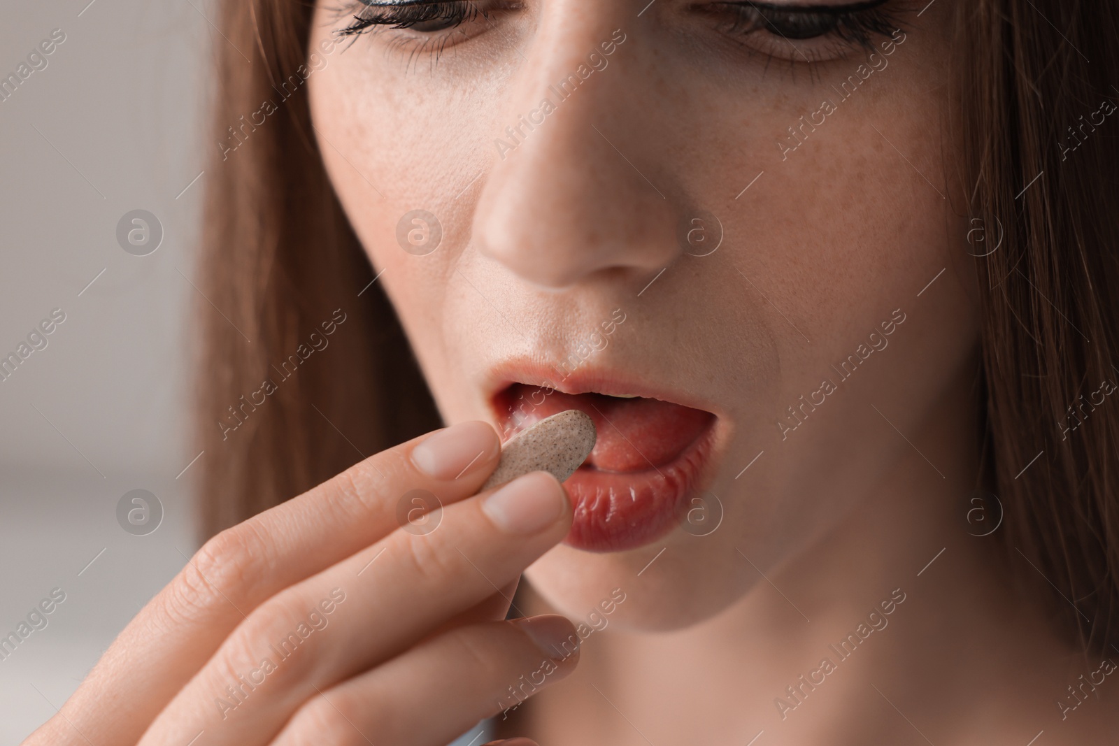 Photo of Woman taking pill on blurred background, closeup