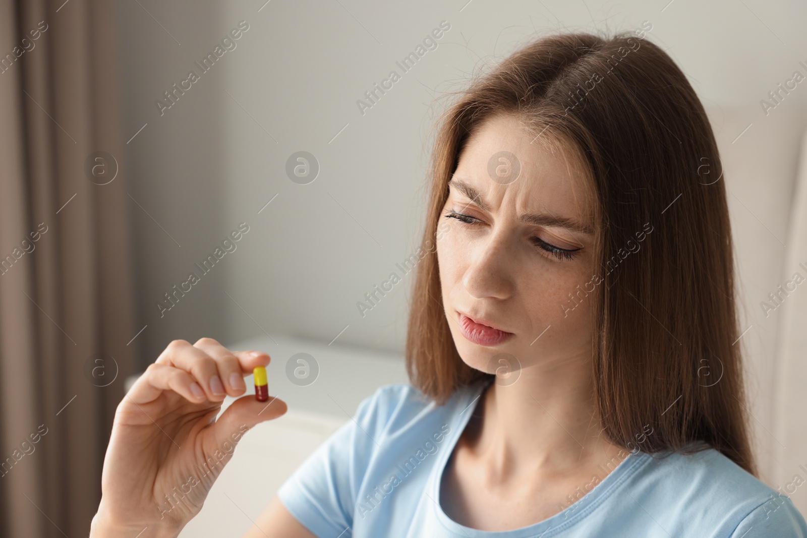 Photo of Beautiful young woman with pill at home