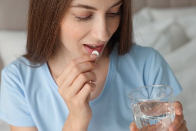 Photo of Woman with glass of water taking pill at home