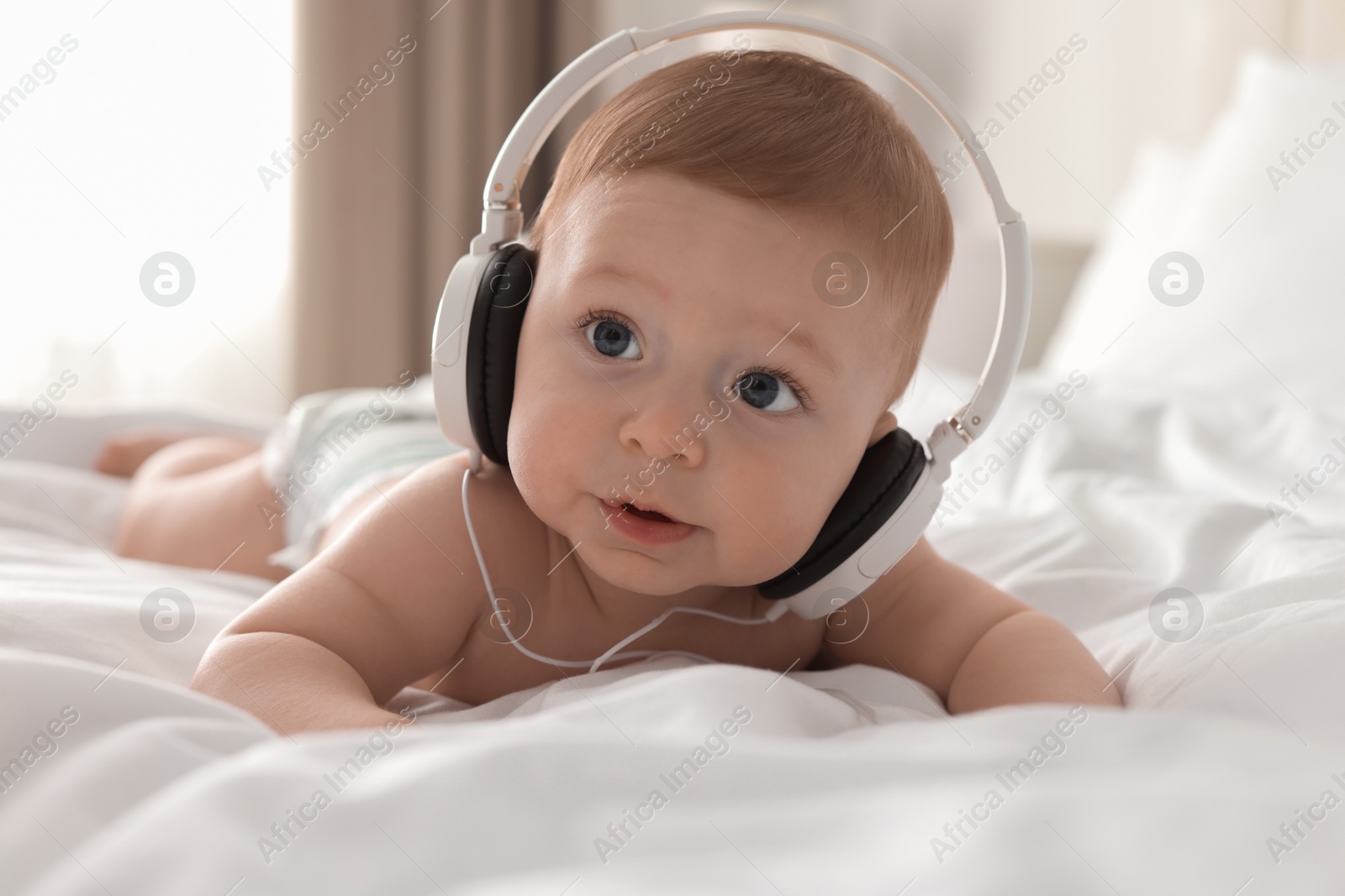 Photo of Cute little baby with headphones on bed at home