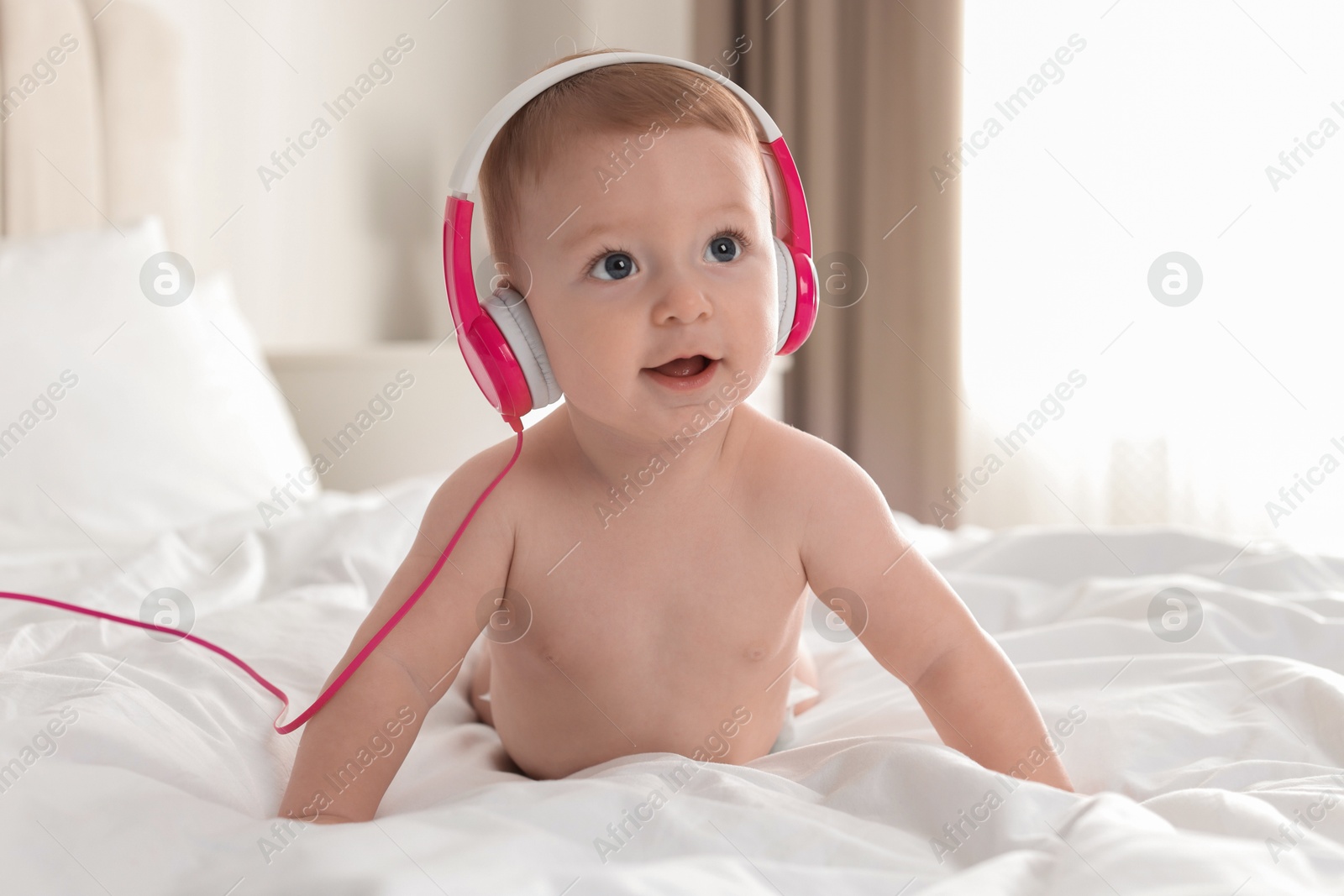 Photo of Cute little baby with headphones on bed at home