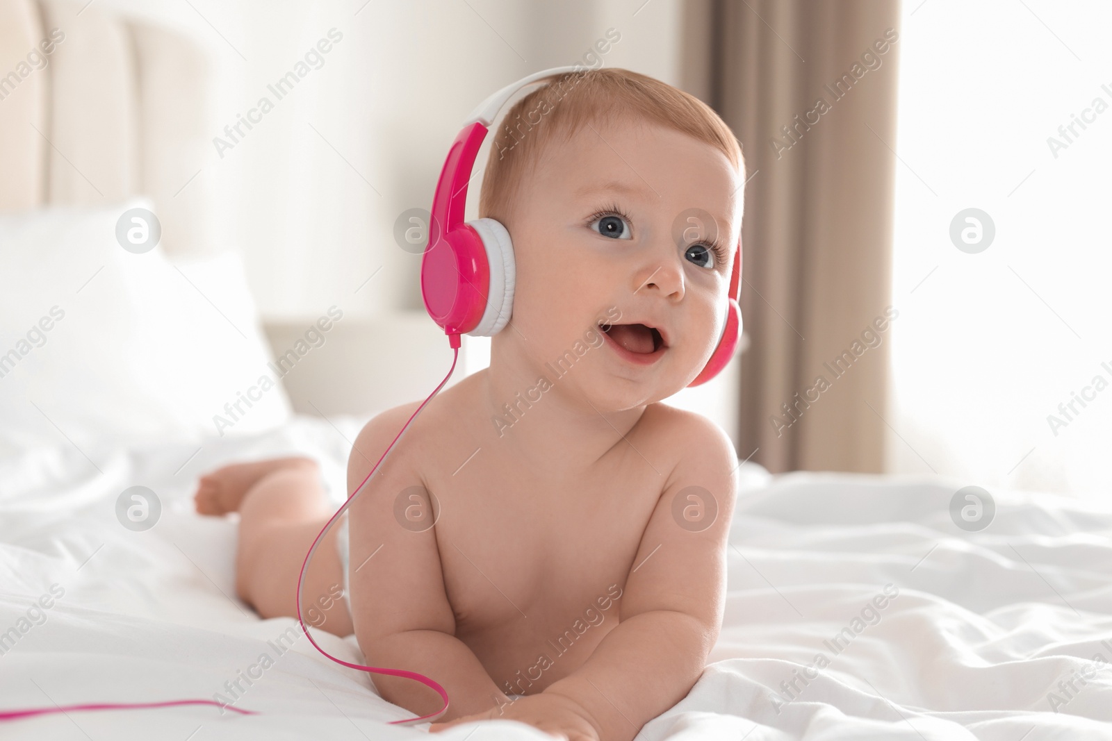 Photo of Cute little baby with headphones on bed at home