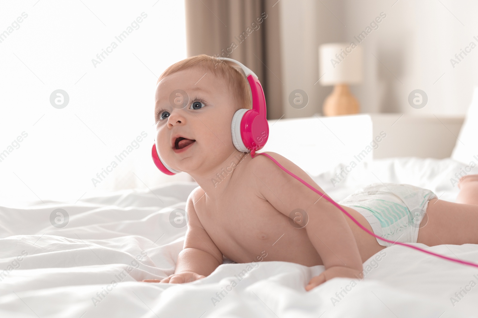 Photo of Cute little baby with headphones on bed at home