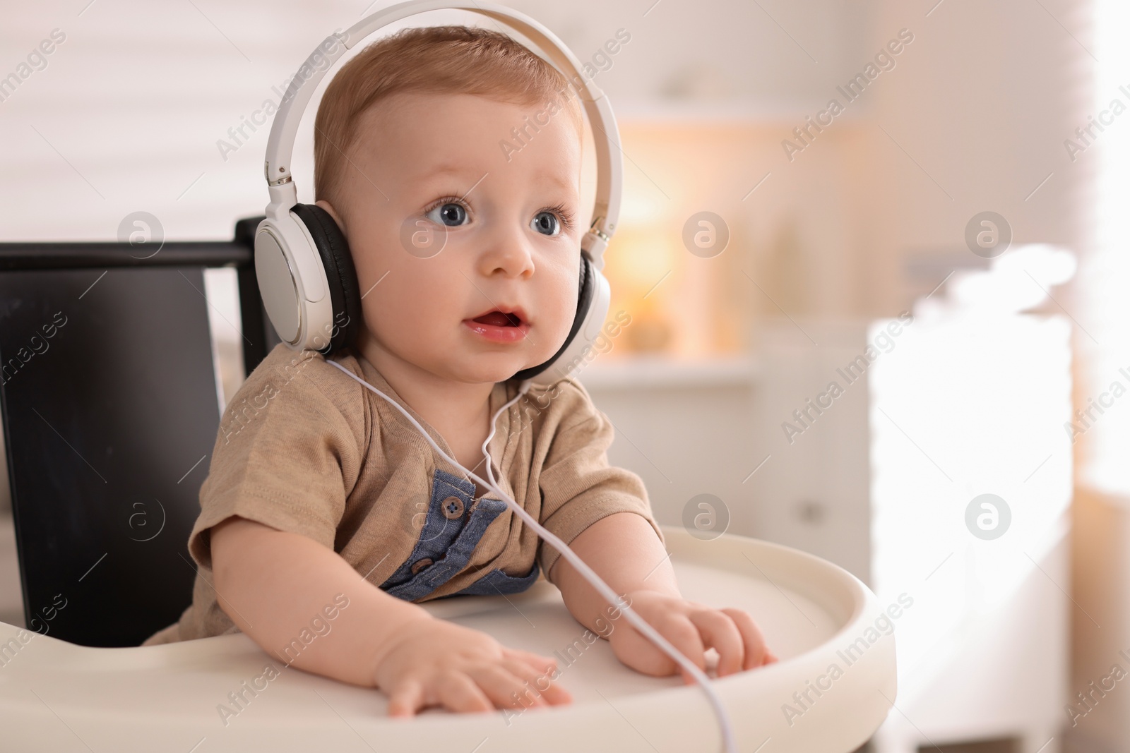 Photo of Cute little baby with headphones on high chair at home, space for text