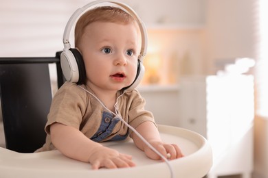 Cute little baby with headphones on high chair at home, space for text