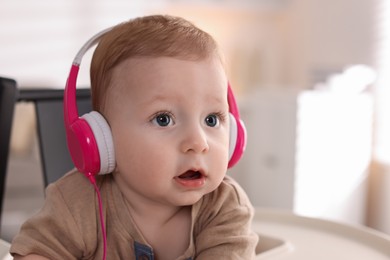 Cute little baby with headphones on high chair at home, space for text