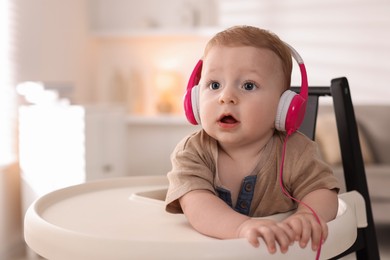 Cute little baby with headphones on high chair at home, space for text