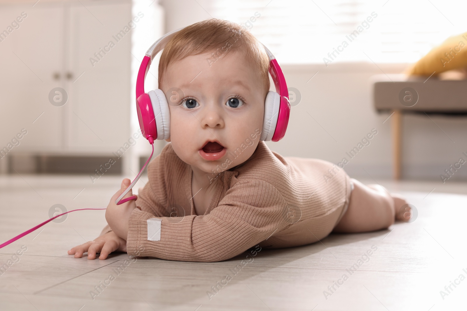 Photo of Cute little baby with headphones on floor at home