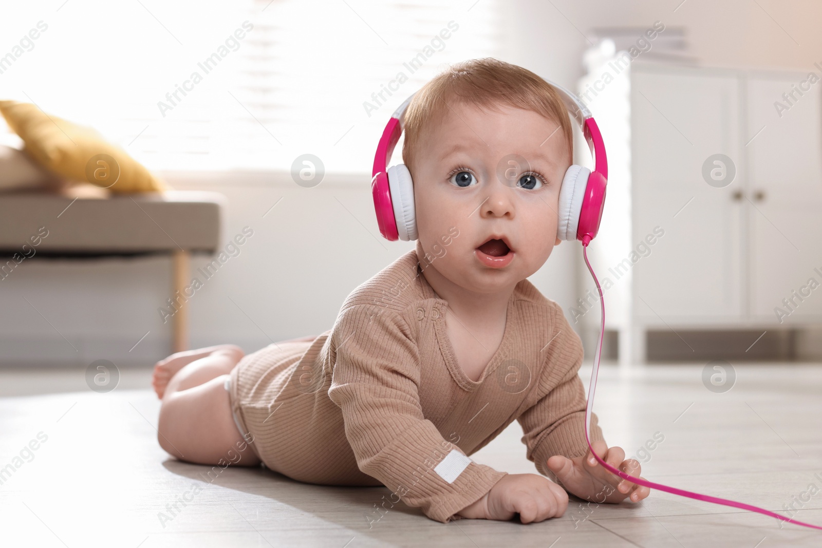 Photo of Cute little baby with headphones on floor at home