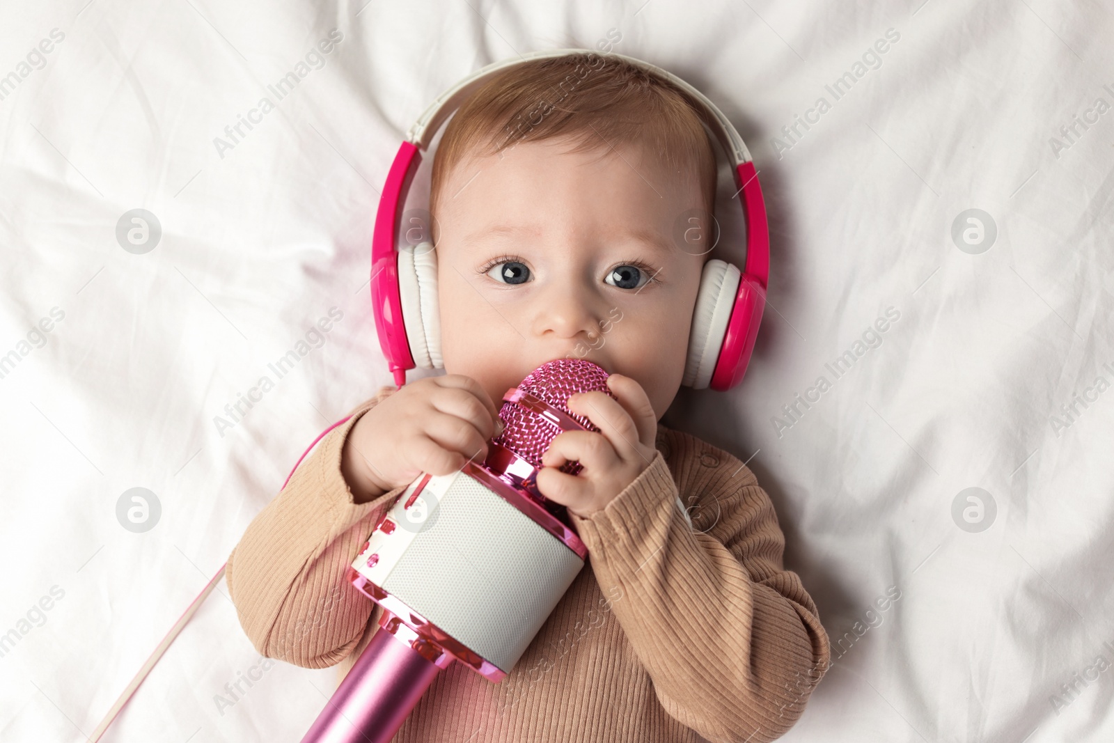 Photo of Cute little baby with headphones and microphone lying on bed, top view