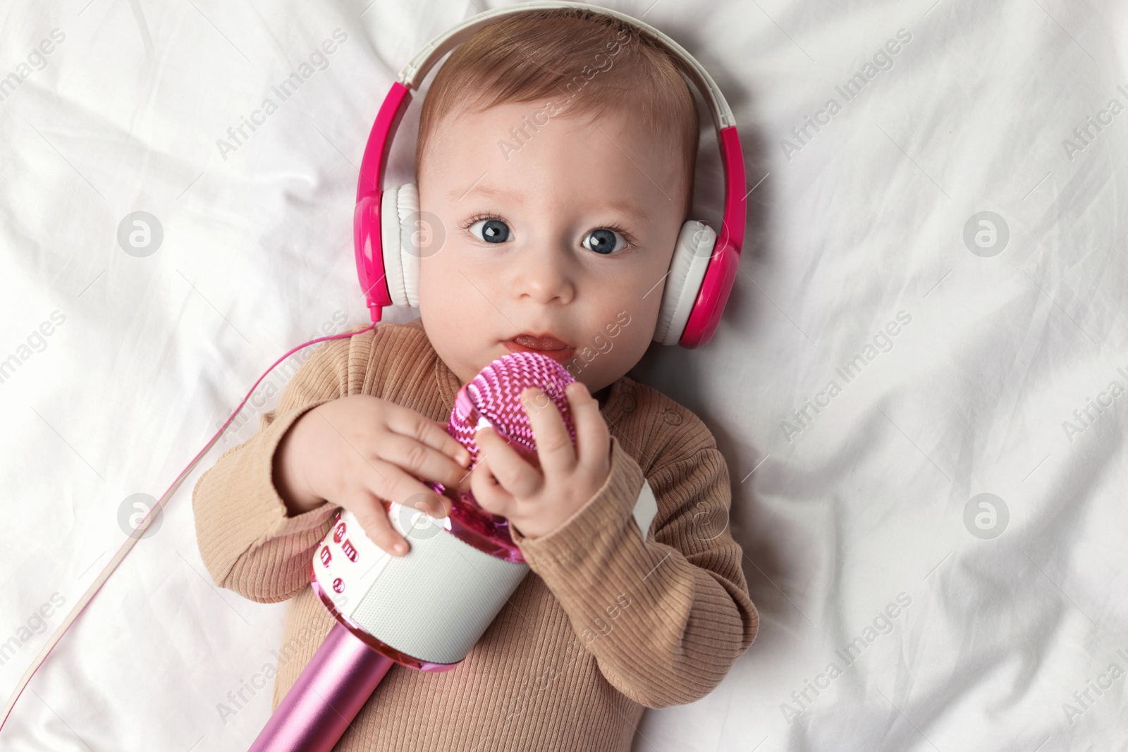 Photo of Cute little baby with headphones and microphone lying on bed, top view