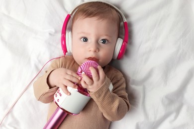 Cute little baby with headphones and microphone lying on bed, top view