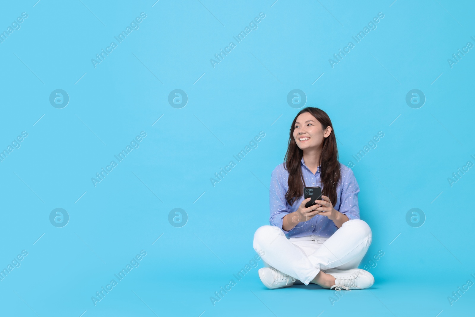 Photo of Smiling woman with smartphone on light blue background. Space for text