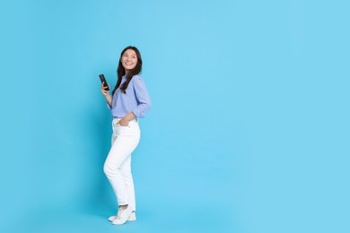 Smiling woman with smartphone on light blue background. Space for text