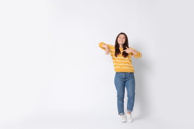 Photo of Smiling woman pointing at something on white background. Space for text