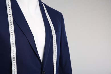 Photo of Male mannequin with elegant suit jacket and measuring tape on grey background, closeup. Space for text