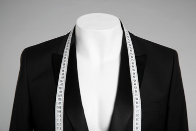 Male mannequin with elegant suit jacket and measuring tape on grey background, closeup