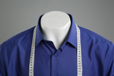 Male mannequin with blue shirt and measuring tape on grey background, closeup