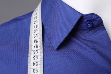 Mannequin with blue shirt and measuring tape on grey background, closeup