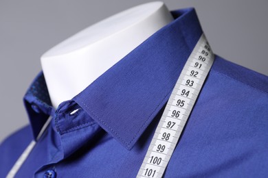 Mannequin with blue shirt and measuring tape on grey background, closeup