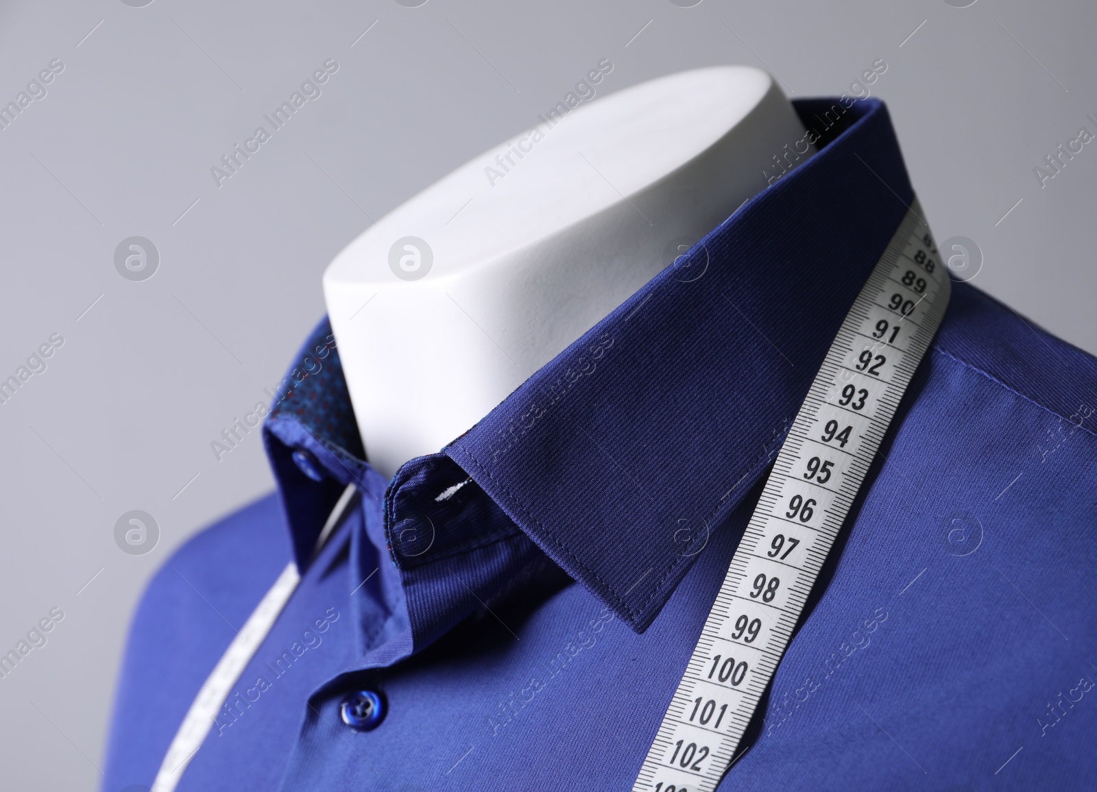 Photo of Mannequin with blue shirt and measuring tape on grey background, closeup