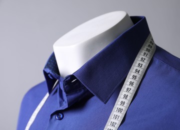 Mannequin with blue shirt and measuring tape on grey background, closeup