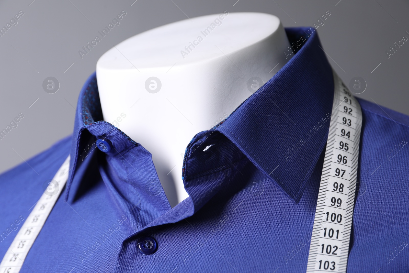 Photo of Mannequin with blue shirt and measuring tape on grey background, closeup