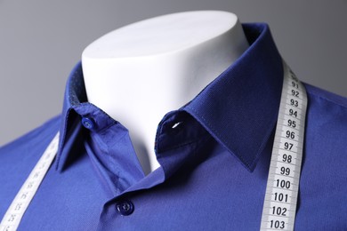 Mannequin with blue shirt and measuring tape on grey background, closeup