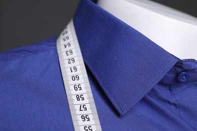 Mannequin with blue shirt and measuring tape on grey background, closeup