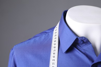 Male mannequin with blue shirt and measuring tape on grey background, closeup