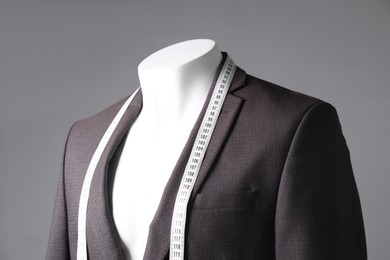 Male mannequin with brown jacket and measuring tape on grey background, closeup