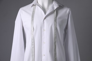 Male mannequin with white shirt and measuring tape on grey background, closeup